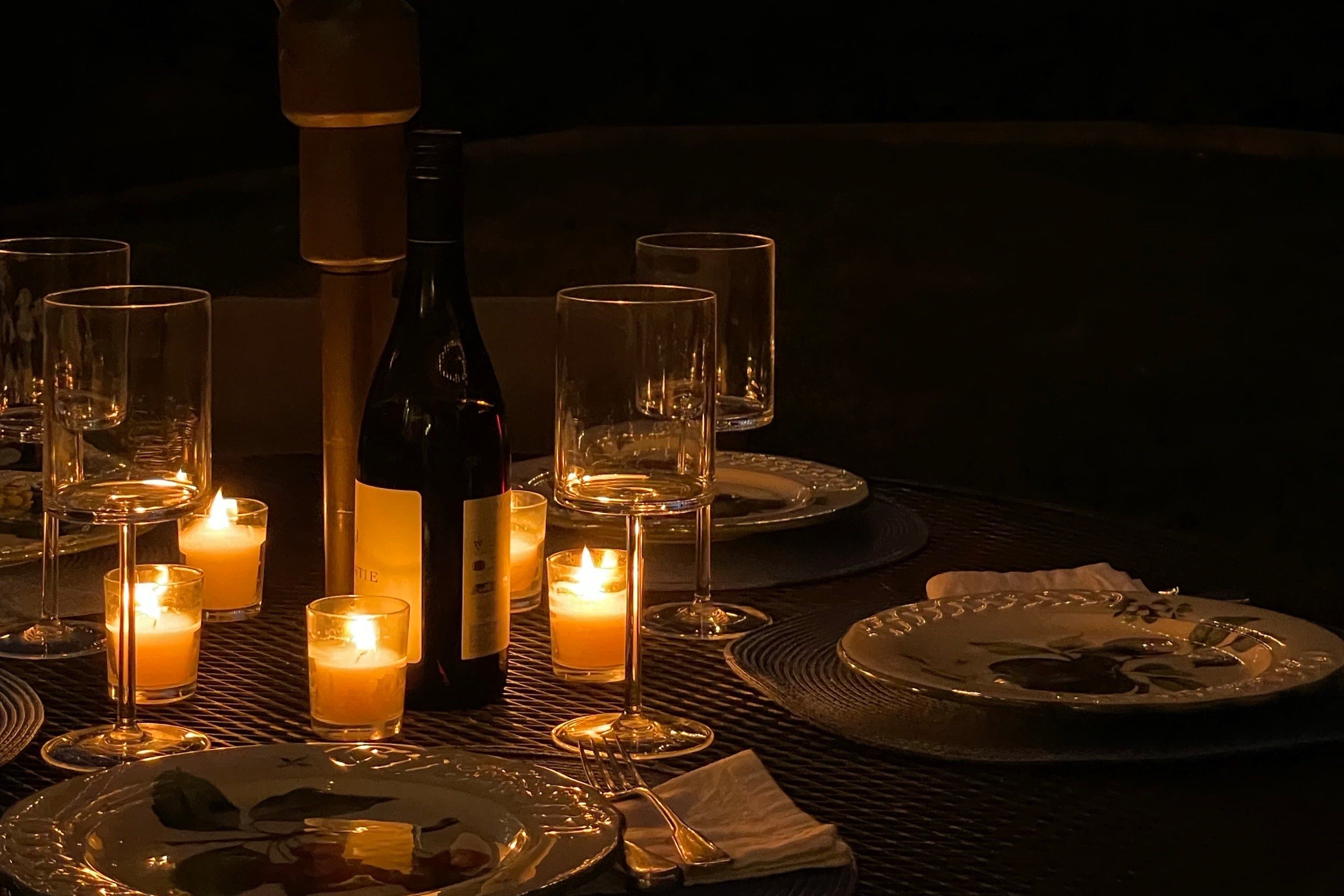 Dining table set for two with candles and a bottle of wine at night.